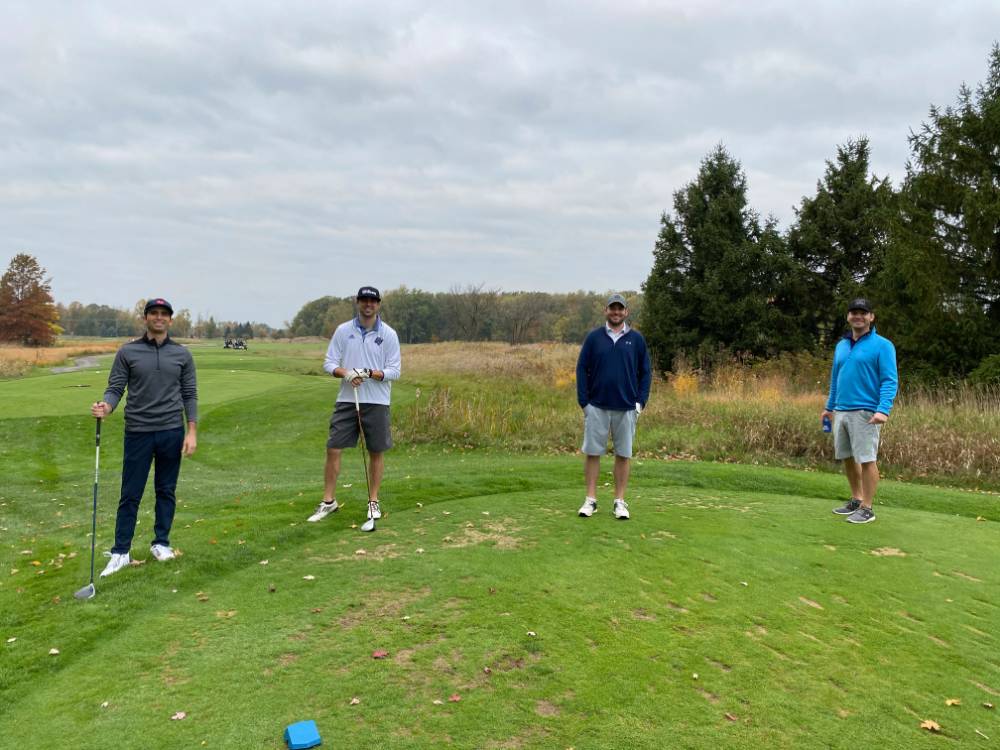 Four alumni standing together on golf course